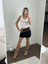 Bota estilo texana de caña media, confeccionada en gamuza color beige. Presenta un diseño slouchy con arrugas naturales, punta fina y taco cuadrado de madera. Incluye costuras decorativas en la puntera y detalles en cuero liso en la parte superior de la caña.