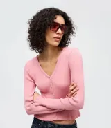 Cardigan de punto texturizado color rosado, con escote en V, cierre frontal por botones, mangas largas y acabado con volados sutiles en el ruedo y los puños.
