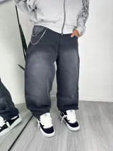 Pantalón de jean estilo baggy, color gris oscuro con efecto lavado, de corte holgado y tiro medio. Incluye cadena metálica decorativa sujeta a la cintura.