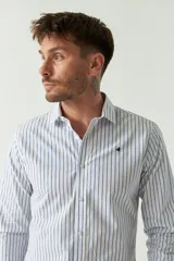 Camisa de hombre de corte slim fit, confeccionada en algodón con diseño de rayas verticales finas en tonos claros. Presenta cuello clásico, cierre frontal con botones y logo bordado en el pecho.