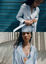 Camisa de popelina celeste a rayas, de corte oversize, con cuello camisero, mangas largas y aplicaciones de pedrería y lentejuelas brillantes distribuidas por toda la prenda.