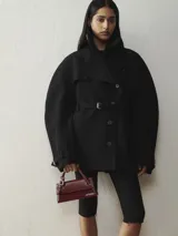 Bolso estructurado de cuero liso color negro, con asa superior reforzada, detalle de hebilla metálica dorada y logo de la marca en letras doradas en la parte frontal.