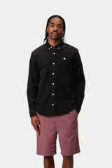 Camisa de manga larga Carhartt WIP modelo Madison Fine Cord, confeccionada en pana de algodón negra, con cuello abotonado, cierre frontal de botones y pequeño logo bordado en blanco en el pecho izquierdo.
