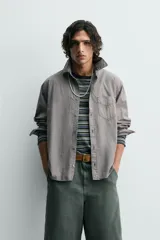 Camisa blanca de algodón con corte relajado, cuello solapa, manga larga con puño abotonado y bolsillo de plastrón en el pecho. Presenta bajo asimétrico con aberturas laterales y cierre frontal de botonadura.