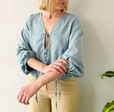 Blusa celeste con escote en V, lazo en el escote y mangas largas abullonadas con puños elásticos.