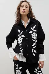 Camisa de denim negro con estampa floral blanca, cuello camisero, cierre frontal con botones y mangas largas.