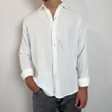 Camisa de manga larga confeccionada en lino, color blanco, con cuello clásico y cierre frontal de botones.