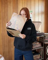 Canguro oversize color negro con capucha y bolsillo frontal tipo canguro. Presenta un pequeño logo bordado en color blanco en el pecho.