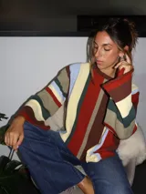 Sweater tejido a mano con terminaciones en crochet, de silueta oversize y mangas acampanadas. Presenta un diseño de rayas verticales multicolores en tonos tierra, rojo, azul y crema.