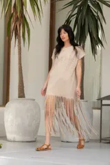 Vestido corto color beige de algodón, con cuello redondo, mangas cortas y flecos en el ruedo. Presenta tachas plateadas en el frente.