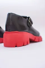 Guillermina de cuero negra con suela tractorada roja y hebilla dorada.