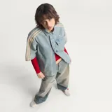 Camisa de jean de manga corta Adidas, confeccionada en 100% algodón, con diseño inspirado en la ropa de trabajo, cierre frontal con broches a presión, cuello camisero, un bolsillo en el pecho con solapa y las clásicas tres tiras de la marca en las mangas.