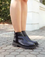 Botinetas de cuero negro con suela track dentada. Presentan un diseño de caña baja con paneles laterales elásticos y cierre lateral, combinando texturas de cuero liso y texturizado.