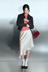 Falda midi de tejido satinado con estampado de lunares negros sobre fondo beige. Presenta un diseño de tiro medio con cintura elástica y un bajo con corte asimétrico.