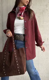 Sobrecamisa de pana color bordó, con cuello camisero, cierre frontal de botones y mangas largas con puños. Presenta una textura acanalada característica de la pana.