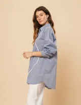 Camisa celeste de algodón con corte oversized, botones frontales a tono y vivos blancos ondulados en el frente.