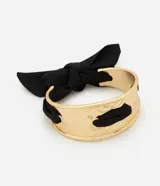 Pulsera rígida ancha de metal dorado, con detalles de tejido y un lazo negro entrelazado.