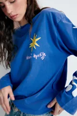 Remera oversize de manga larga color azul, con efecto lavado, cuello redondo y detalle de estampación inspirada en Henri Matisse con una estrella amarilla en el pecho y formas abstractas blancas en la manga.
