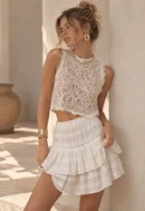 Top corto sin mangas de encaje blanco con diseño floral y cuello alto.