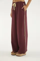 Pantalón bordó de corte amplio y relajado, con cintura elástica y cordón ajustable amarillo. Presenta bolsillos laterales y una línea lateral en contraste de color amarillo.