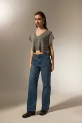 Chaleco de punto gris con cuello en V, diseño sin mangas y corte cropped. Presenta apliques de tachas metálicas plateadas distribuidas por toda la parte frontal y borde acanalado en el ruedo.