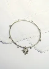 Brazalete esclava de plata con apliques esféricos a lo largo del aro y dije colgante en forma de corazón.