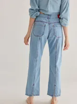 Jean de corte recto confeccionado en denim azul oscuro, con costuras a la vista en color rojo contrastante. Presenta un diseño de tiro alto con bolsillos frontales y cierre de botón.