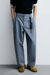 Pantalón de hombre color azul grisáceo, estilo balloon fit, confeccionado en mezcla de algodón y lino. Presenta pliegues en el delantero, cierre frontal con botón y cremallera, bolsillos laterales y bolsillos traseros de plastrón.