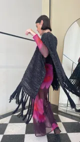 Ruana tejida de color negro con sutiles destellos plateados, diseño de líneas verticales y terminación con flecos largos en los extremos.