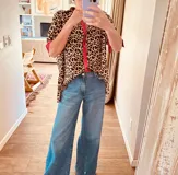 Camisa de manga corta con estampado animal print y detalles en rojo intenso en cuello y puños. Corte holgado y cierre frontal con botones.