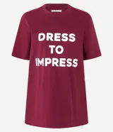 Remera color borgoña de algodón, con cuello redondo y mangas cortas. Estampa frontal con la frase "Dress to Impress" en letras mayúsculas blancas.