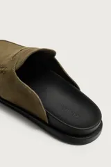Zueco de hombre fabricado en piel con acabado serraje en color marrón claro. Presenta un diseño destalonado con detalle de antifaz en el empeine, horma redonda y suela plana a contraste.