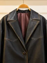 Blazer de cuero vacuno en color negro con efecto gastado y costuras a la vista. Presenta solapas clásicas, cierre frontal con dos botones y bolsillos laterales con solapa.