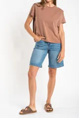 Remera de algodón color mostaza/naranja quemado, con cuello redondo y mangas cortas. Presenta un diseño con costuras externas visibles en los hombros y laterales, dándole un aspecto desestructurado.