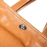 Cartera tipo bandolera grande de cuero color suela, con doble asa de mano y correa larga ajustable y extraíble. Presenta cierre superior con broche giratorio metálico y logo de la marca grabado en el frente.