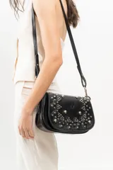 Bandolera de cuero negro con estructura rígida, tapa frontal decorada con tachas metálicas plateadas colocadas a mano y correa larga ajustable.