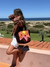 Bolso tote artesanal de cuero, reversible. Un lado presenta un diseño patchwork con figuras geométricas delimitadas por pasamanería en tonos tierra, naranja, amarillo y rosado. El reverso es liso.