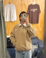 Buzo de pana color beige con cuello polo, cierre frontal parcial y forro interior de corderito. Presenta diseño oversized, bolsillos laterales y puños elásticos.
