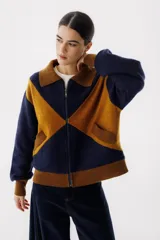 Chaqueta bomber azul marino con paneles color mostaza en forma de rombos. Tiene cuello tipo camisa, cierre frontal con cremallera, bolsillos de parche y puños y bajo acanalados en color marrón.