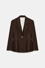 Blazer marrón confeccionada en hilatura con mezcla de lino, con cuello solapa, manga larga, bolsillos con solapa en el delantero y cierre frontal con un botón. Cuenta con forro interior en color blanco contrastante.