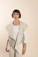 Chaleco sin mangas de tejido de lana fina sin teñir, con diseño circular y bloques de color beige y marrón. Presenta un cuello amplio y solapa que permite usarlo como chaleco largo o capa corta.