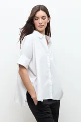 Camisa blanca de corte oversized, confeccionada en algodón, con cuello clásico, cierre frontal de botones y mangas cortas con vuelta.