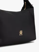 Cartera tipo hobo de Tommy Hilfiger confeccionada en nailon brillante color negro. Presenta un diseño minimalista con el monograma TH metálico en dorado en la parte frontal, cierre superior con cremallera, asa superior fija y correa cruzada extraíble con detalles en contraste.