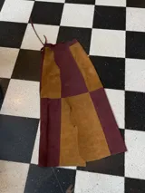 Falda larga de cuero en diseño de paneles bicolor, combinando tonos marrón y bordó. Presenta cintura ajustable con lazo y un diseño de borde lateral irregular con tajos.