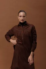 Camisa de cuero ovino color marrón, con diseño oversize, cuello camisero, cierre frontal con broches y detalle de flecos en el pecho. Presenta mangas largas con puños.