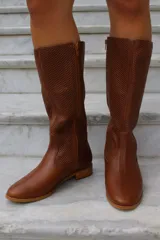 Bota de caña alta confeccionada en cuero, con diseño de textura perforada en la parte superior de la caña y puntera lisa. Cuenta con suela plana y taco bajo.