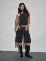 Bermuda de denim negro con tiro medio, bolsillos frontales decorados con strass y apliques de pedrería, y terminación desmechada en las piernas.