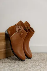 Botas cortas de cuero negro con paneles traseros de gamuza, cierre lateral y detalle de correa con hebilla metálica en el tobillo.