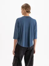 Remera de silueta relajada confeccionada en tela de punto suave. Presenta escote redondo, mangas 3/4, recorte estratégico en la espalda y tajos laterales que aportan movimiento y una caída fluida.