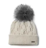 Gorro de lana tejido con diseño de trenzas, color beige, con borde acanalado y pompón de piel sintética en tono gris. Incluye una pequeña placa metálica con el logo de la marca en el frente.